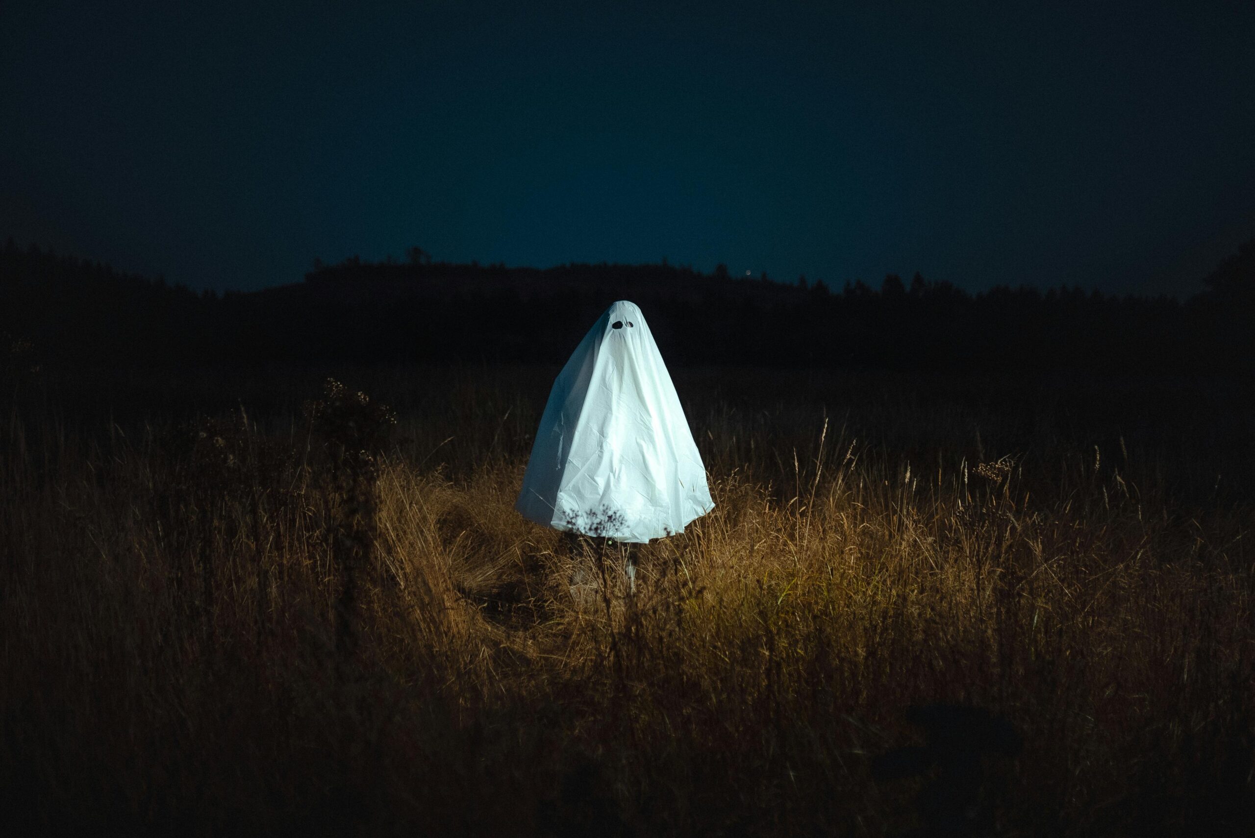 Eerie ghost in a white sheet standing alone in a dark field under a night sky. Perfect for Halloween imagery.